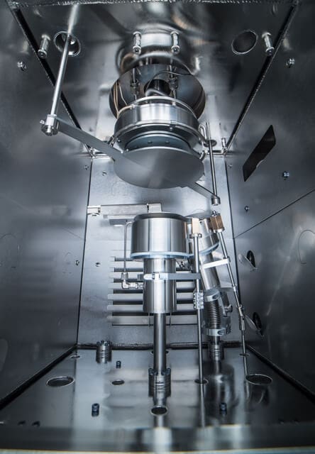 alt = interior view of a sputter heated stage. The equipment has various metal components such as rods, plates and cylinders in a metal chamber. This demonstrates the precise and advanced processes Angstrom Engineering manufactures.